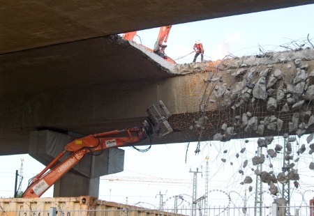 Seitlich aus der Brücke hängende Stahlseile werden per Hand mit einem Schweißbrenner durchtrennt.